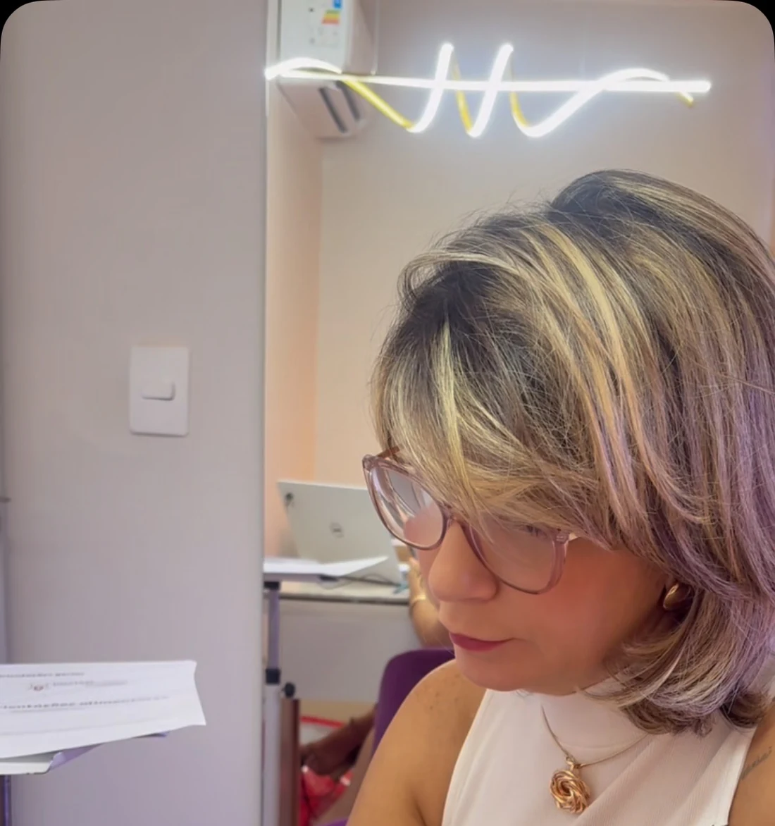 Lucília Lima em sua mesa na clínica, com o letreiro neon da marca ao fundo